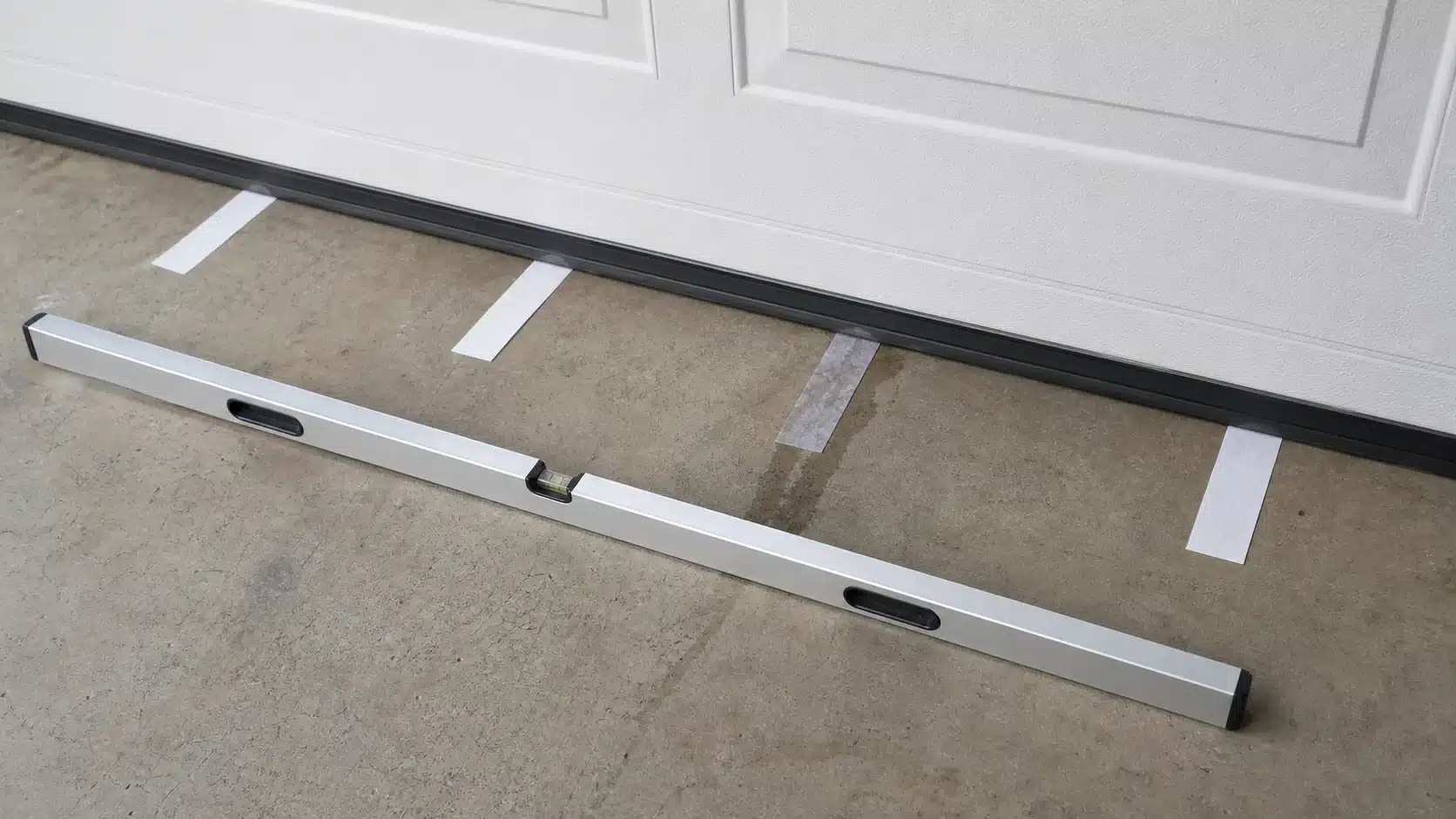 Absorbent strips and a straightedge being used to identify a garage threshold low spot and first wet point