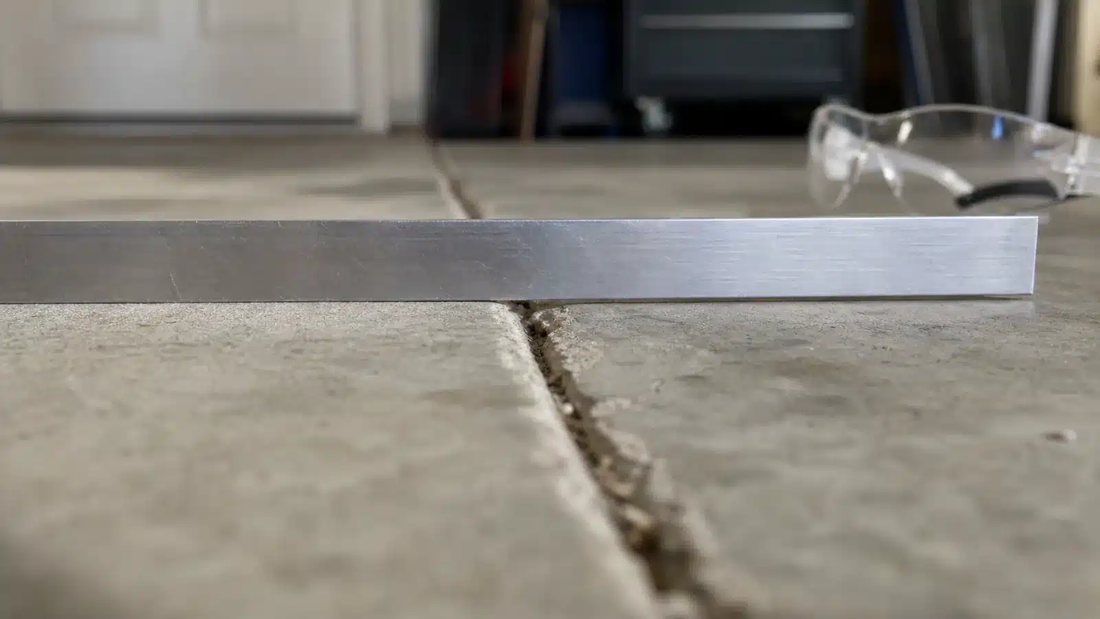 Straightedge spanning a garage floor crack with one concrete slab edge higher than the other
